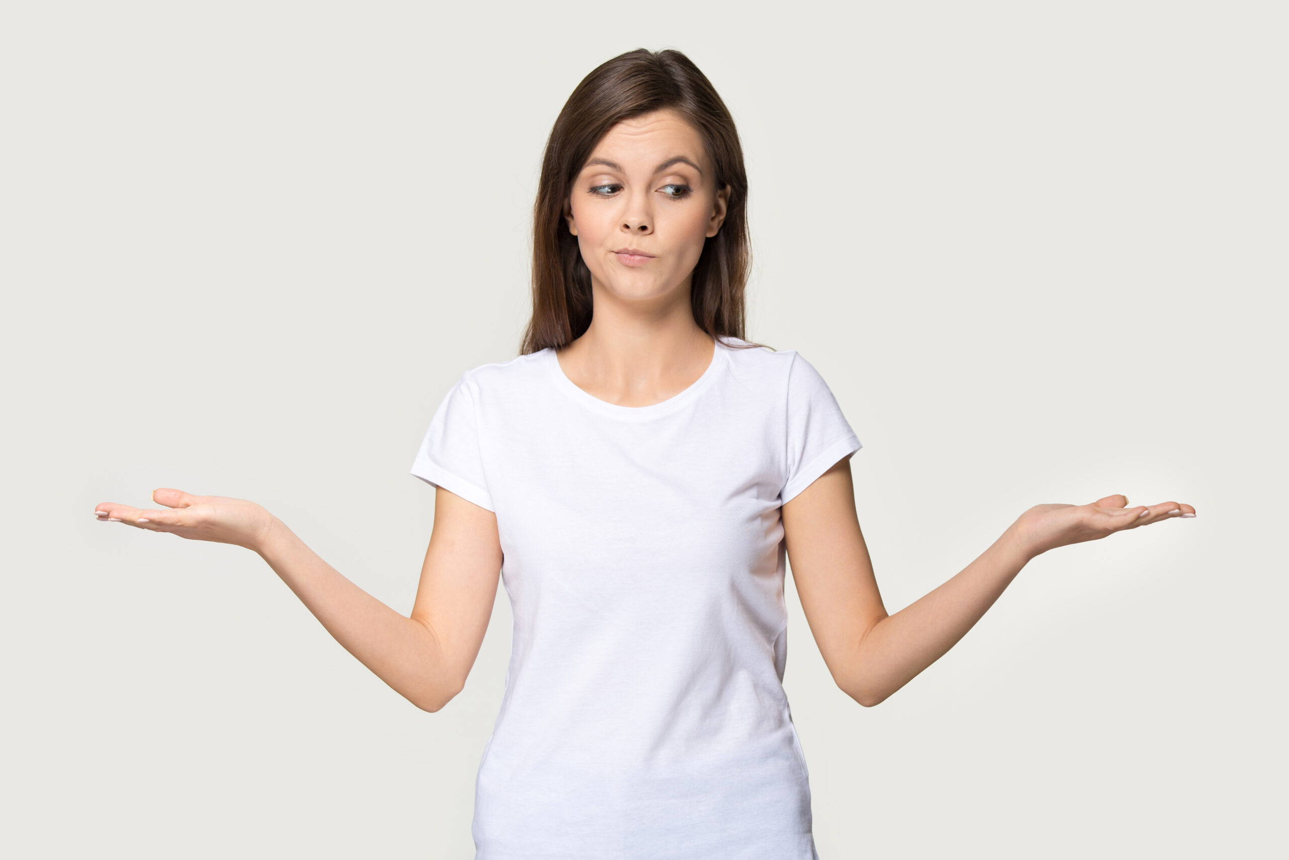 Young woman wearing white t-shirt with her hands up on each side, implying a choice she has to make.